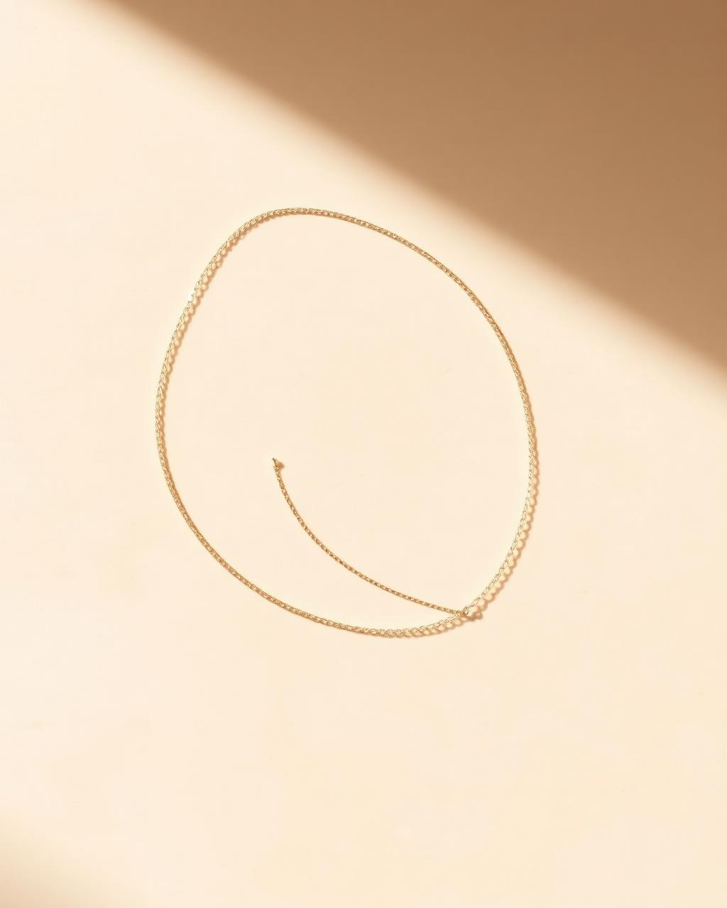A fine gold chain draped on pale warm stone.